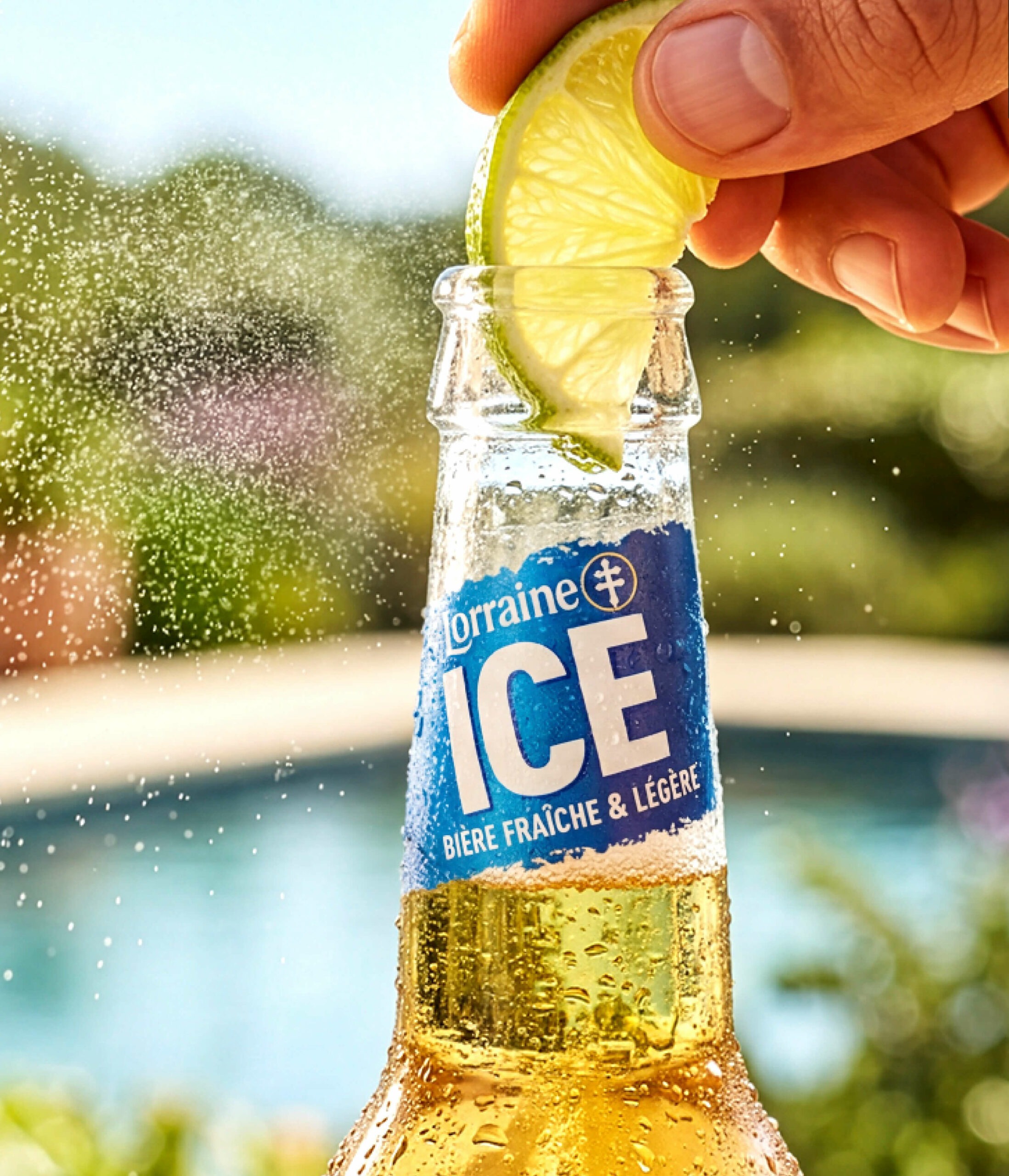 Tranche de citron déposée dans une bouteille de bière Lorraine Ice, décor avec une piscine, ensoleillé